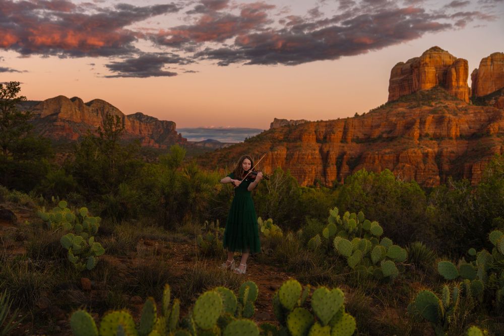 Dramatic sunset illuminates red rock formations in a desert landscape with golden light and dramatic clouds.