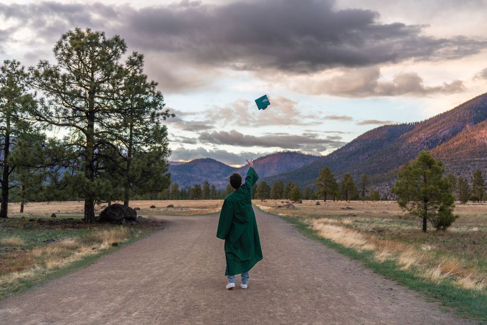 Person throwing objects into dramatic cloudy sky on mountain path.