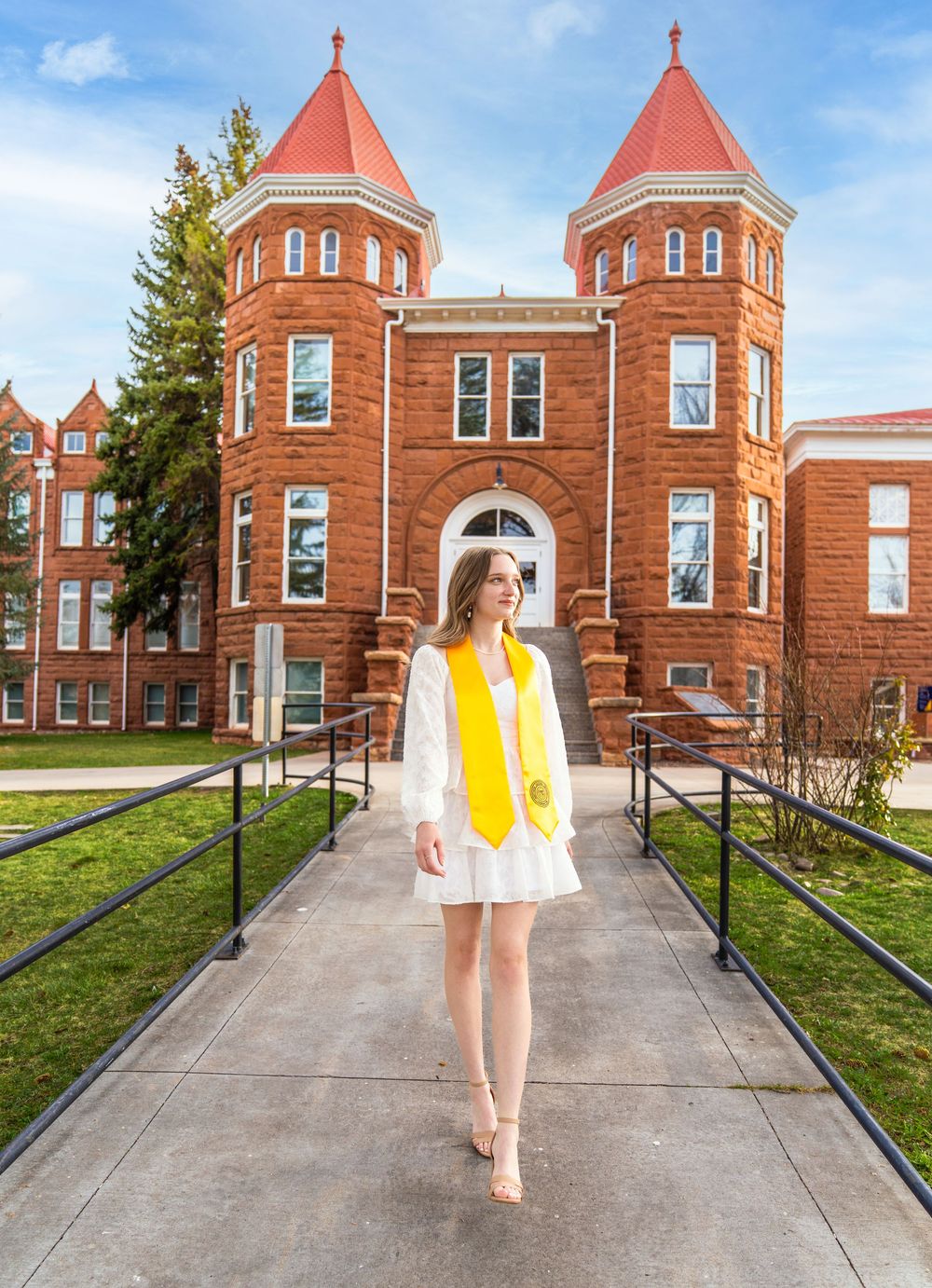 Graduate poses in front of historic red brick university building with turrets and arched windows.