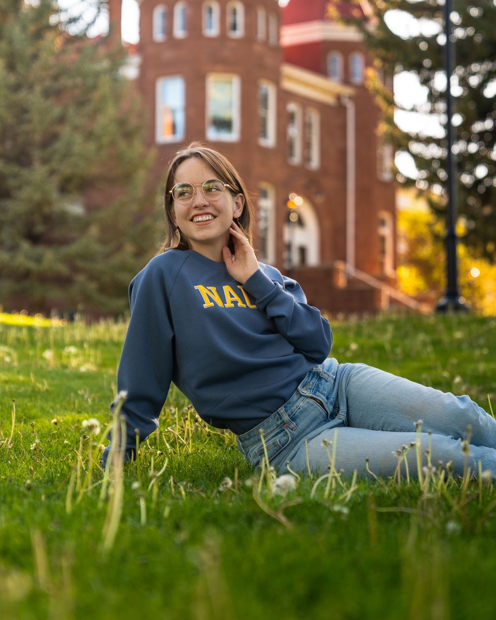 Graduate in NAU sweatshirt relaxes on grass during outdoor campus photo session.
