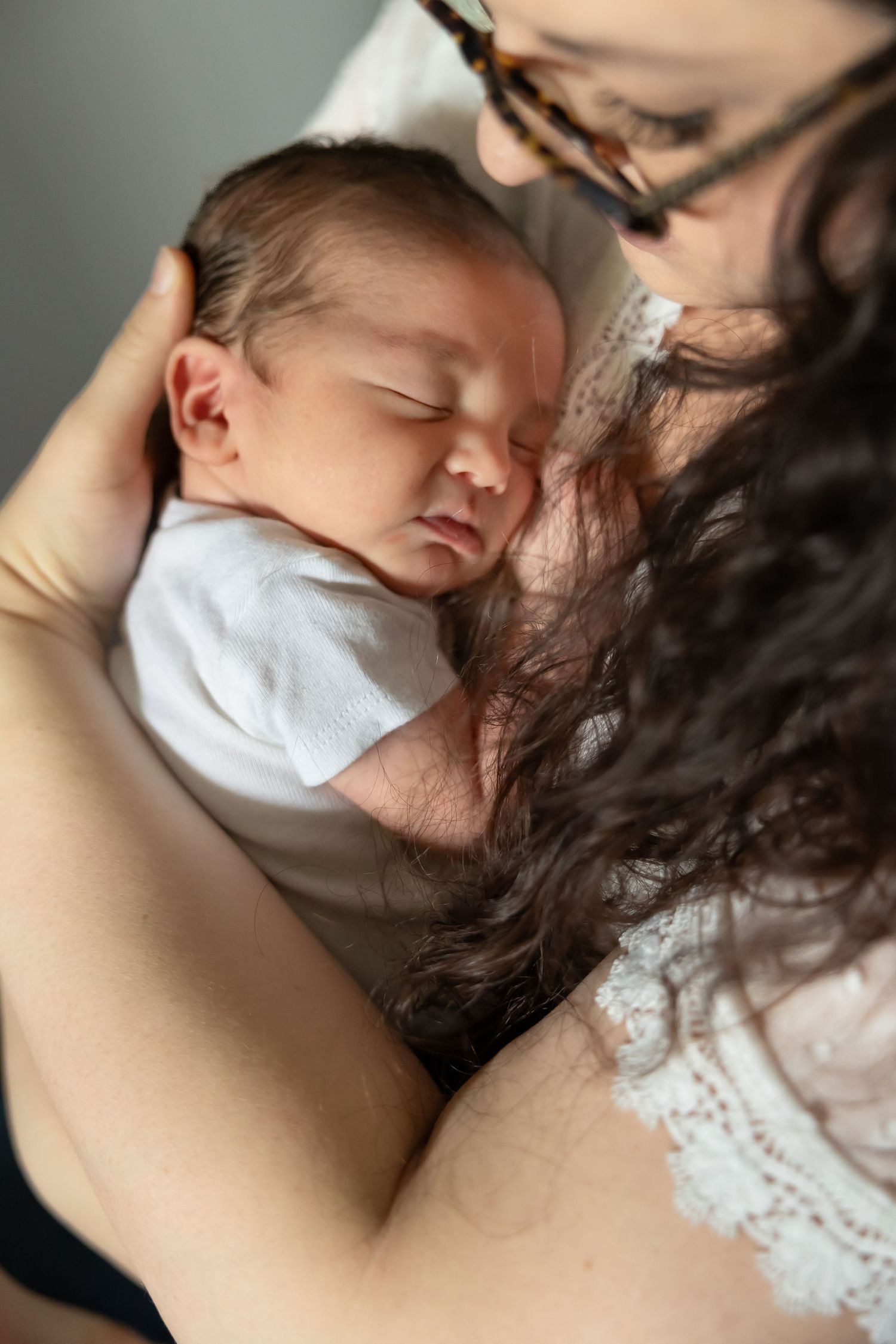 A tender moment between parent and sleeping infant in white clothing against dark background.
