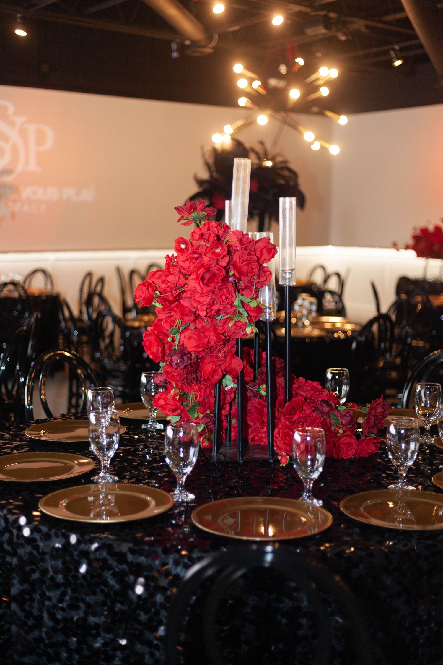 Elegant table setting with vibrant red floral centerpiece, black sequin tablecloth, and crystal glassware at formal event.