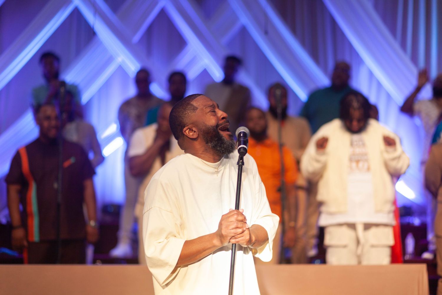 A choir performs on stage in a church with blue lighting and performers dressed in white robes.