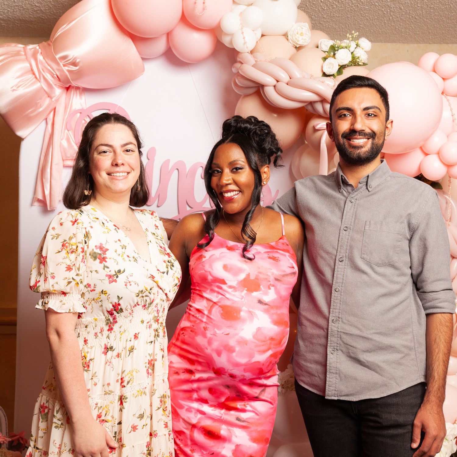 A group of people posing together against a wall with pink balloon decorations in the background.