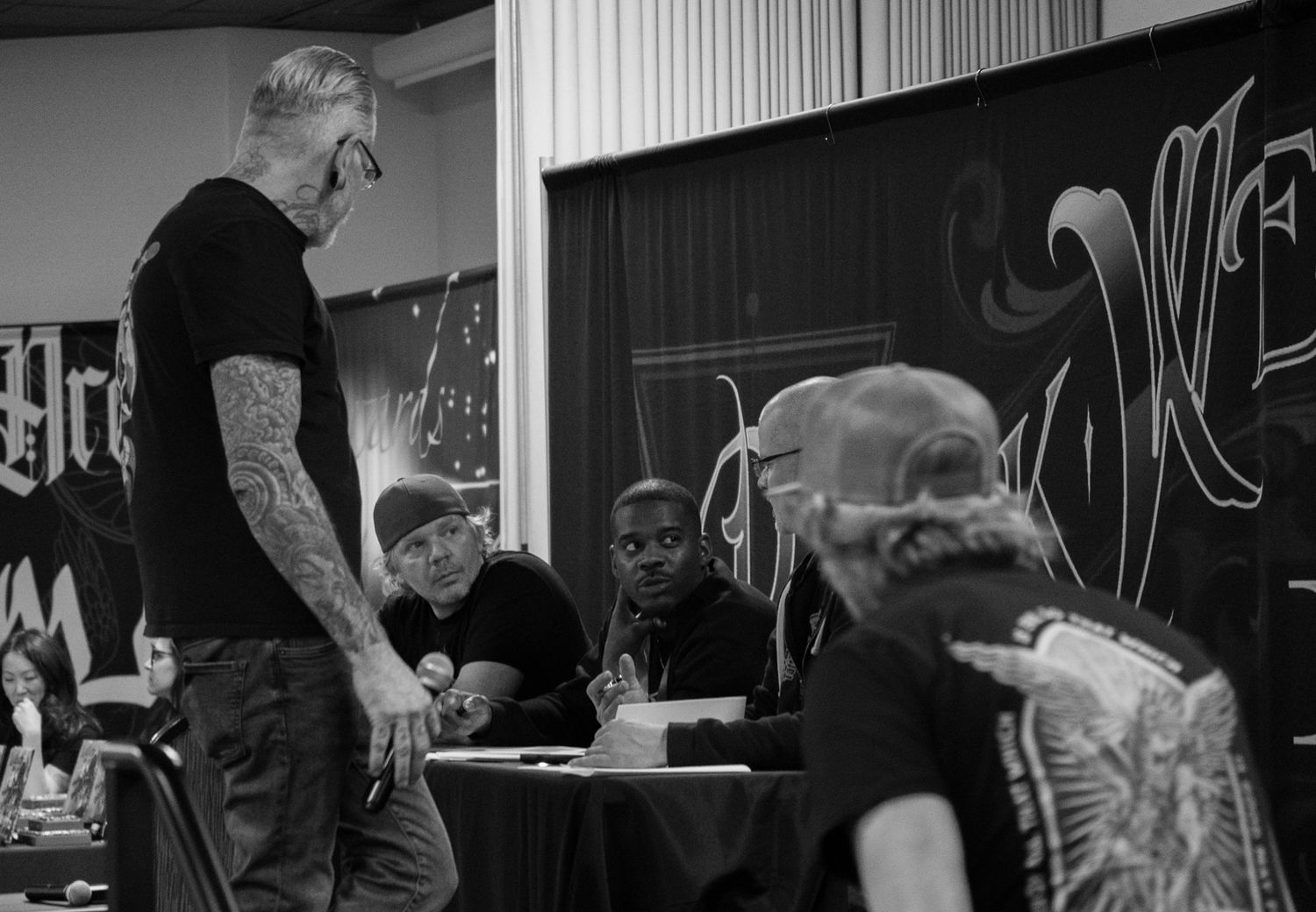 Tattoo artist works meticulously on a client's arm in a professional studio setting with framed artwork on the walls.