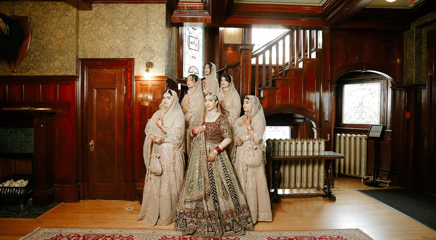 A festive wedding procession with guests in white clothing celebrating on a tree-lined path.