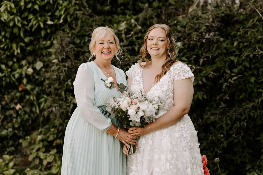 Bridal party in white dresses and burgundy gowns pose joyfully together against a natural outdoor backdrop.