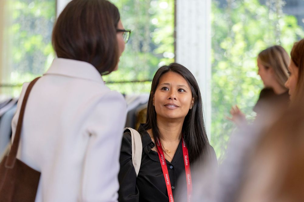 Students engage in conversation in a bright indoor setting with natural light streaming through windows.