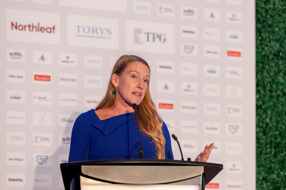 Professional speaker presenting at a business conference with corporate sponsor logos visible in background.