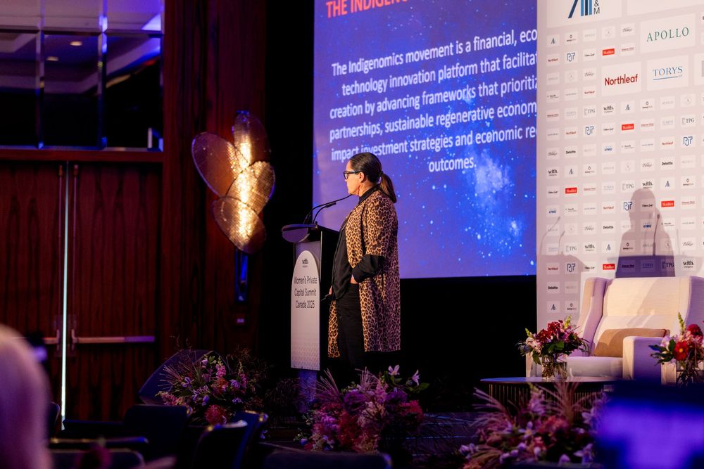 Conference presentation with blue lighting and projected slides on screen showing text and information.