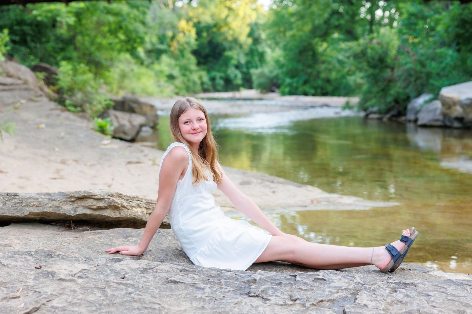 A couple in coordinated blue and gray outfits poses together near a peaceful creek in a natural outdoor setting.