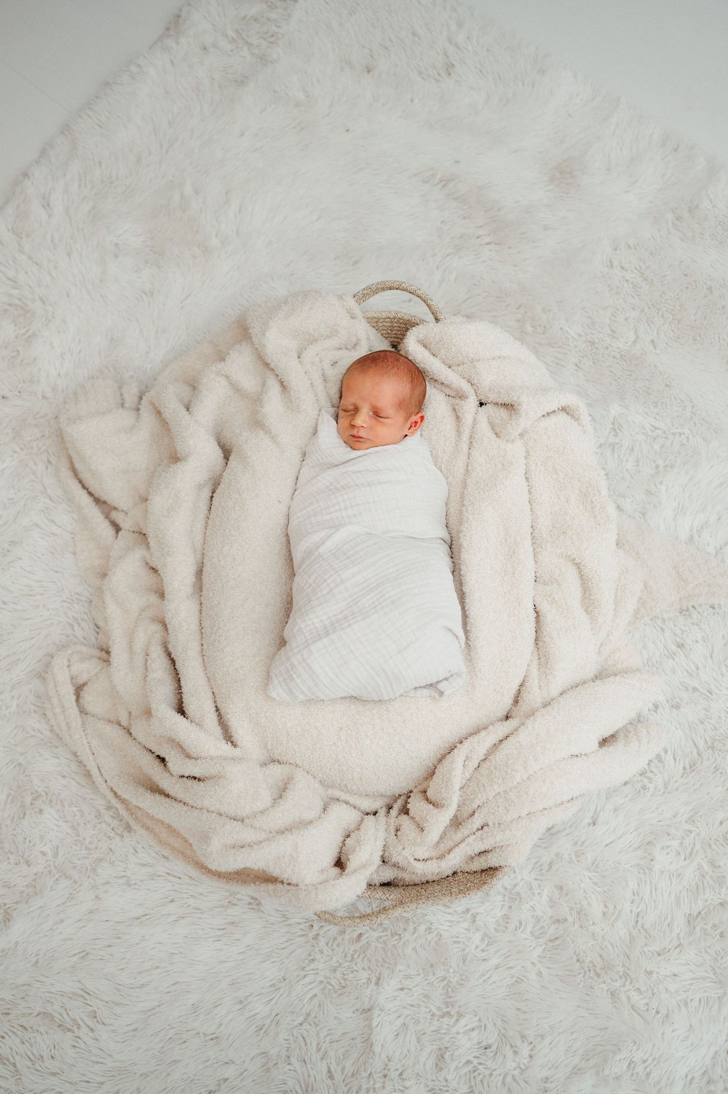Newborn swaddled in white wrap on textured cream backdrop.