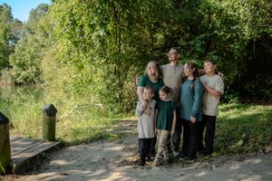 A group of people gather on a nature trail surrounded by lush green trees and foliage on a sunny day.
