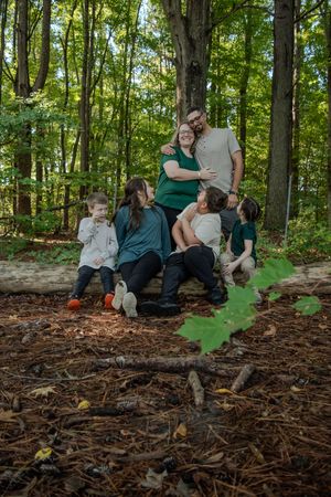 A group sits together on a fallen log in a lush green forest during an autumn day.