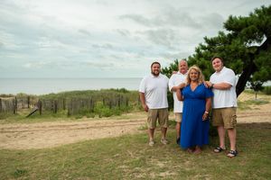 A family wearing blue and white outfits poses together for outdoor beach portraits at sunset.