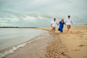 A group walks along a sandy beach shoreline on a cloudy day with waves gently rolling in.