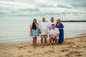A group sits together on a sandy beach with cloudy skies and ocean waves in the background.