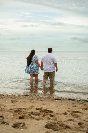 Two people wade into shallow ocean waters at the beach on a cloudy day.
