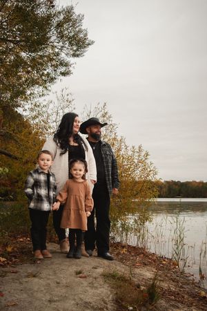 A group poses together on a lakeside path during autumn with fall foliage and water in the background.