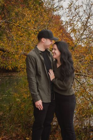 A couple shares an intimate moment against vibrant orange fall foliage by a lake.