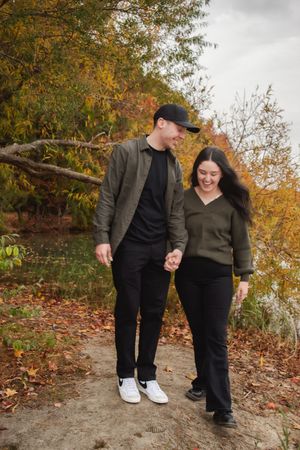 A couple walks together on a path surrounded by autumn trees with golden leaves on a cloudy day.