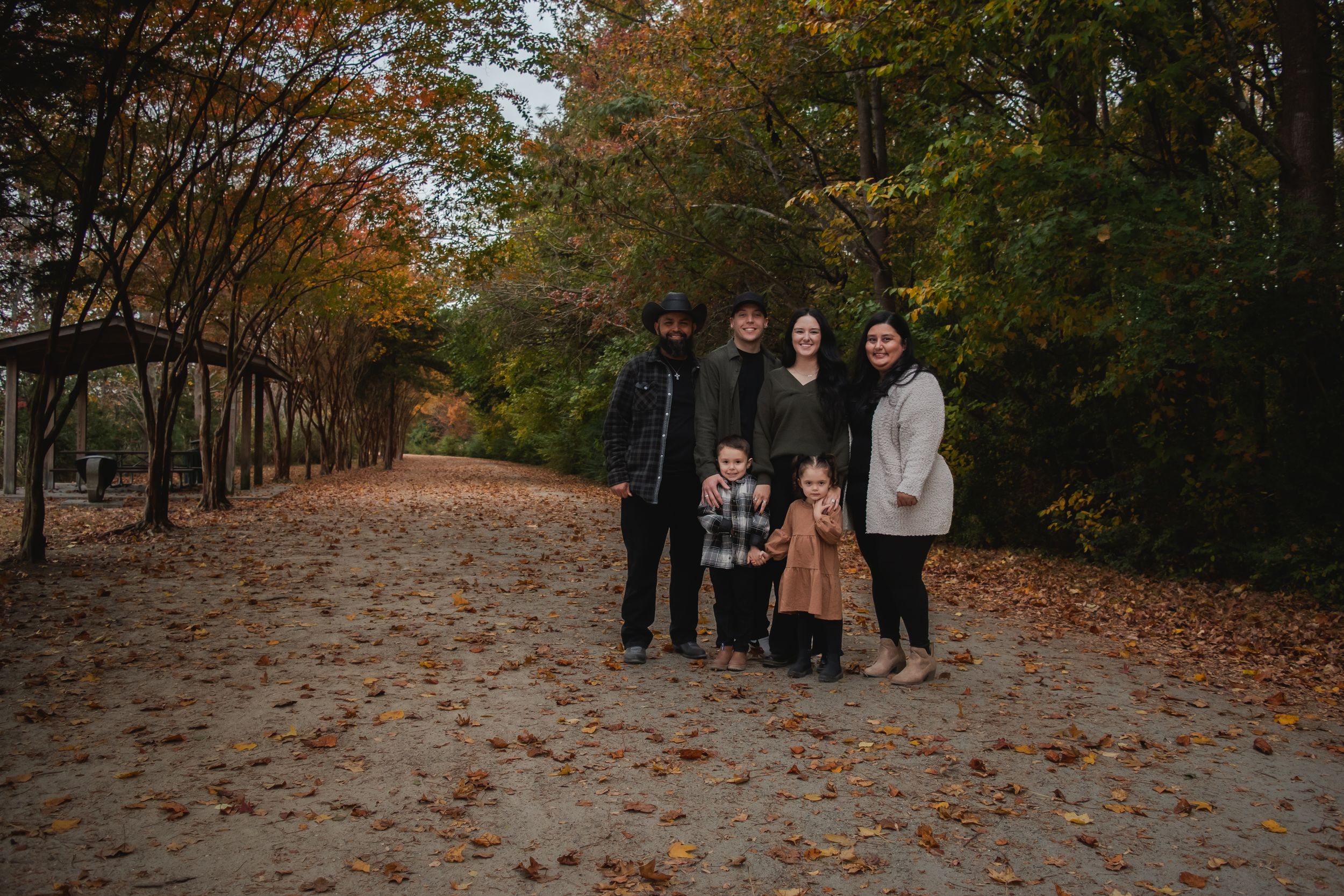 A group walks together on a leaf-covered path through an autumn forest.