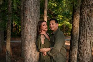 A couple shares intimate moments together while posing among tall pine trees in a forest setting.