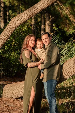 A family shares tender moments together while posing against a large tree trunk in an outdoor nature setting.