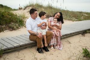 Family sits together on wooden boardwalk at beach during sunset photo session.