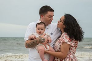 A family shares tender moments together during a beach photoshoot with their baby along the shoreline.