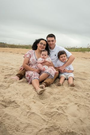 A family relaxes together on a sandy beach, wearing coordinating outfits in a series of casual outdoor portraits.