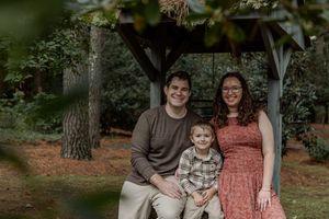 A family in coordinated coral and brown outfits poses together outdoors in a wooded setting.