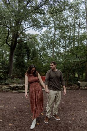 A couple walks together and shares a laugh while exploring a wooded trail on an overcast day.