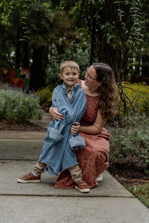 A parent and child share a tender moment together sitting on concrete steps surrounded by greenery in a garden setting.