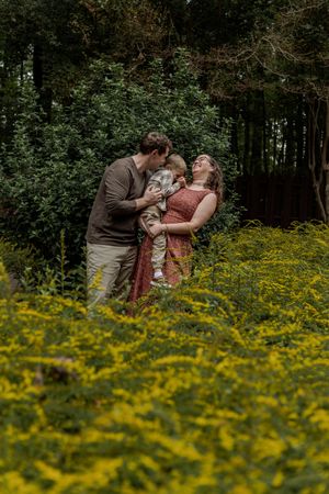 A romantic couple embraces in a field of vibrant yellow wildflowers with a forest backdrop during golden hour.