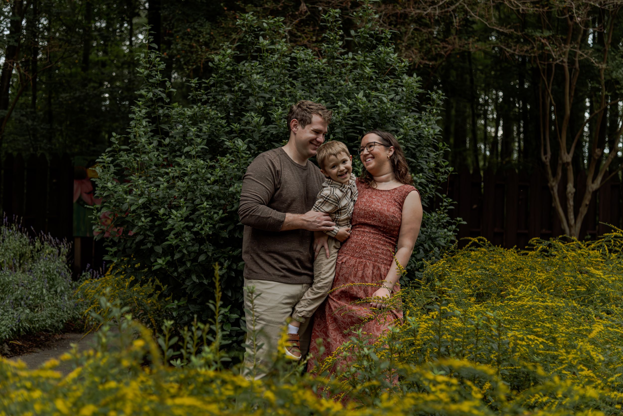 A couple shares a tender moment while standing in a garden with yellow wildflowers and forest backdrop.