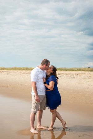 A couple shares a romantic moment on a sandy beach with cloudy skies in the background.