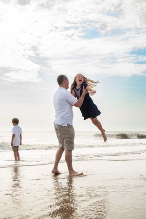 A playful family photoshoot sequence at the beach with jumping and splashing in the ocean waves at sunset.