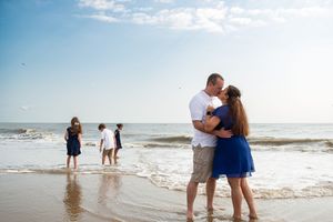 Couple shares romantic moments on a sandy beach at sunset with ocean waves in the background.