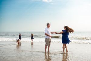 Couple walking hand in hand along the shoreline as waves crash on a sunny beach.