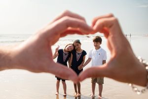 A group of people walk along a sandy beach at sunset while forming a heart shape with their hands.