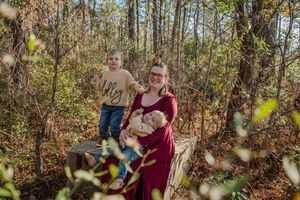 Family portrait session captured in a sunlit autumn forest with warm golden tones and natural foliage surroundings.