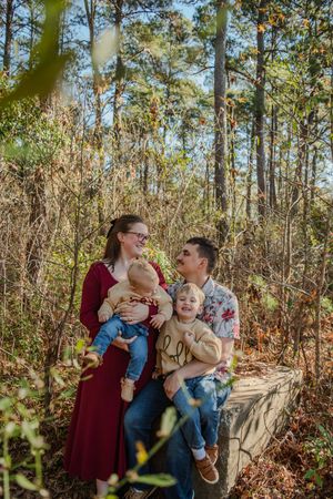 Family enjoying a tender moment together while standing among tall pine trees in an autumn forest setting.