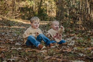 Two young children play and laugh together while sitting in autumn leaves on the ground.
