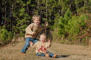 A sequence of candid outdoor photos showing a toddler playing and crawling on a dirt path surrounded by pine trees.