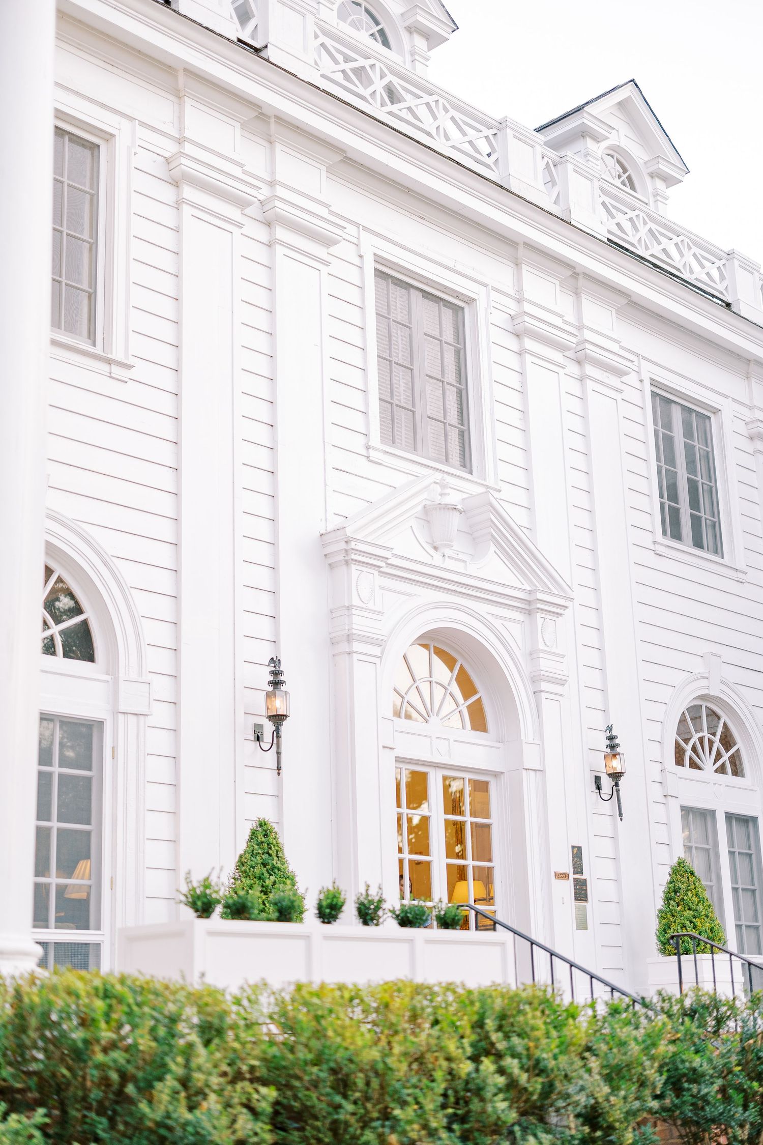 Elegant white mansion with classical architecture featuring arched windows, ornate moldings, and manicured topiary shrubs.