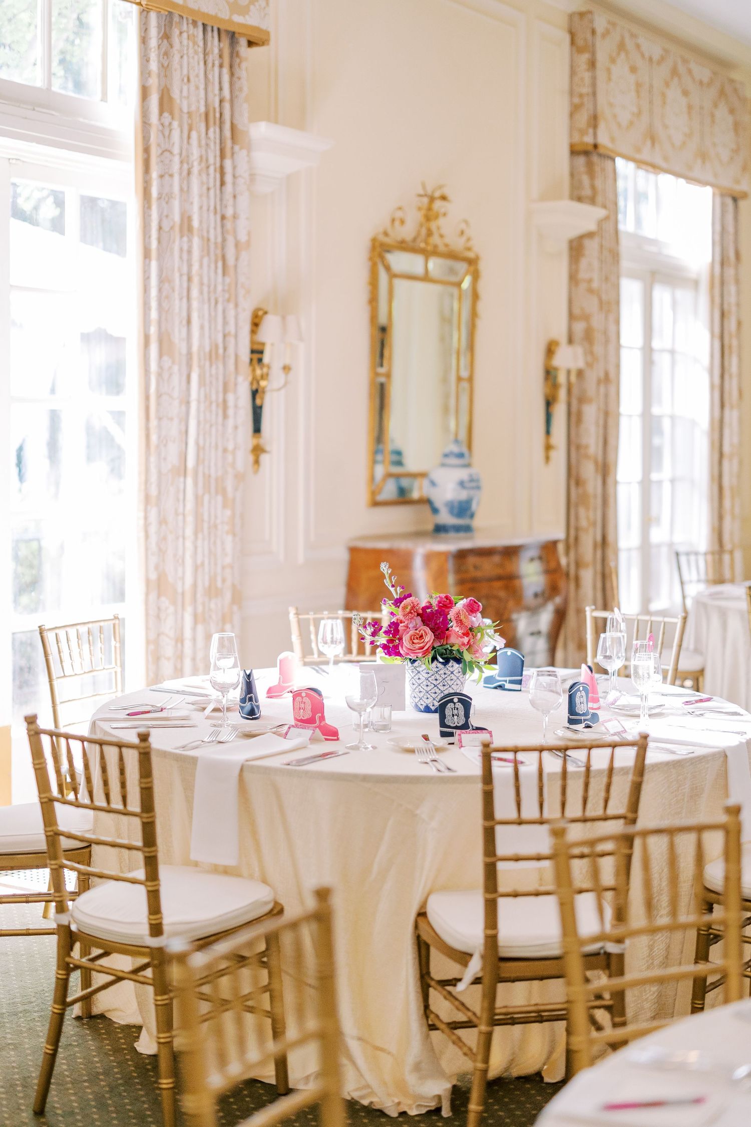 Elegant wedding reception venue with round tables draped in white linens, gold chiavari chairs, and pink floral centerpieces.