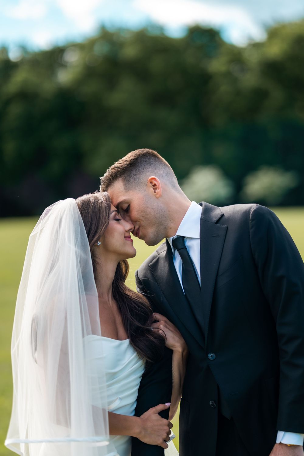 A romantic wedding couple shares tender kisses in a series of photos taken outdoors in a grassy field.