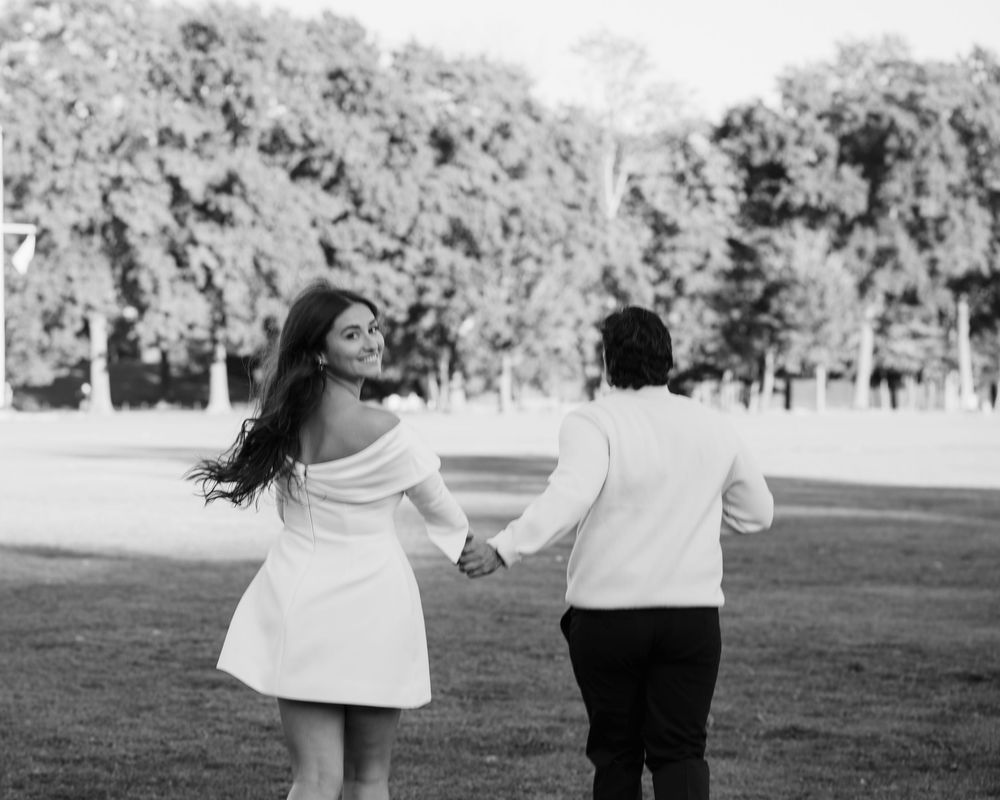 A couple in black and white spins playfully together in a park setting during a romantic photoshoot.