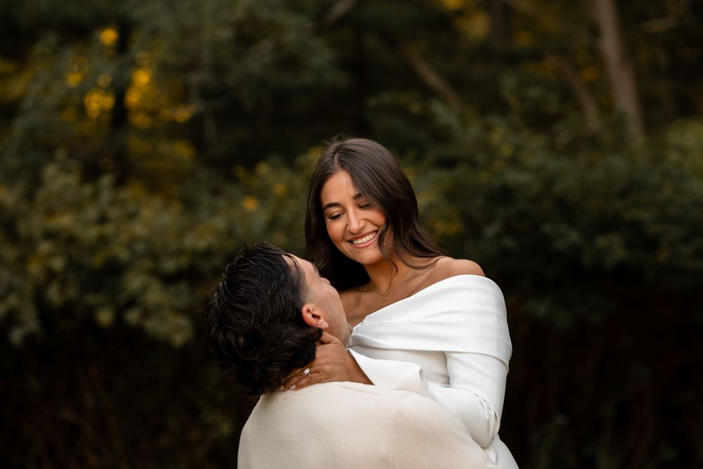 A romantic couple embraces in a natural outdoor setting with soft lighting and foliage in the background.
